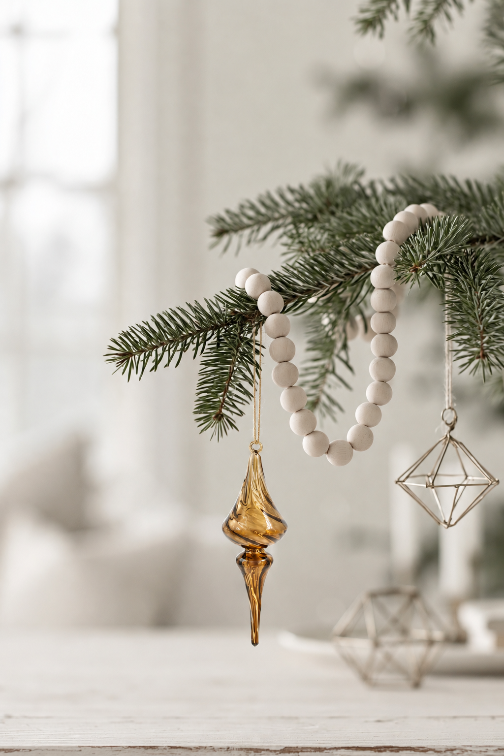 Seraphine glass finial in clear umber hanging on a pine branch with a wooden bead garland