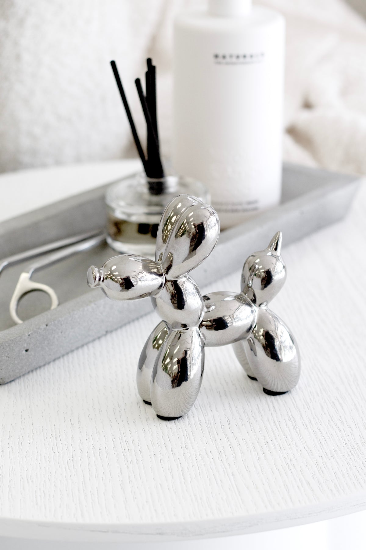 Silver balloon dog sculpture styled on white table beside diffuser and tray