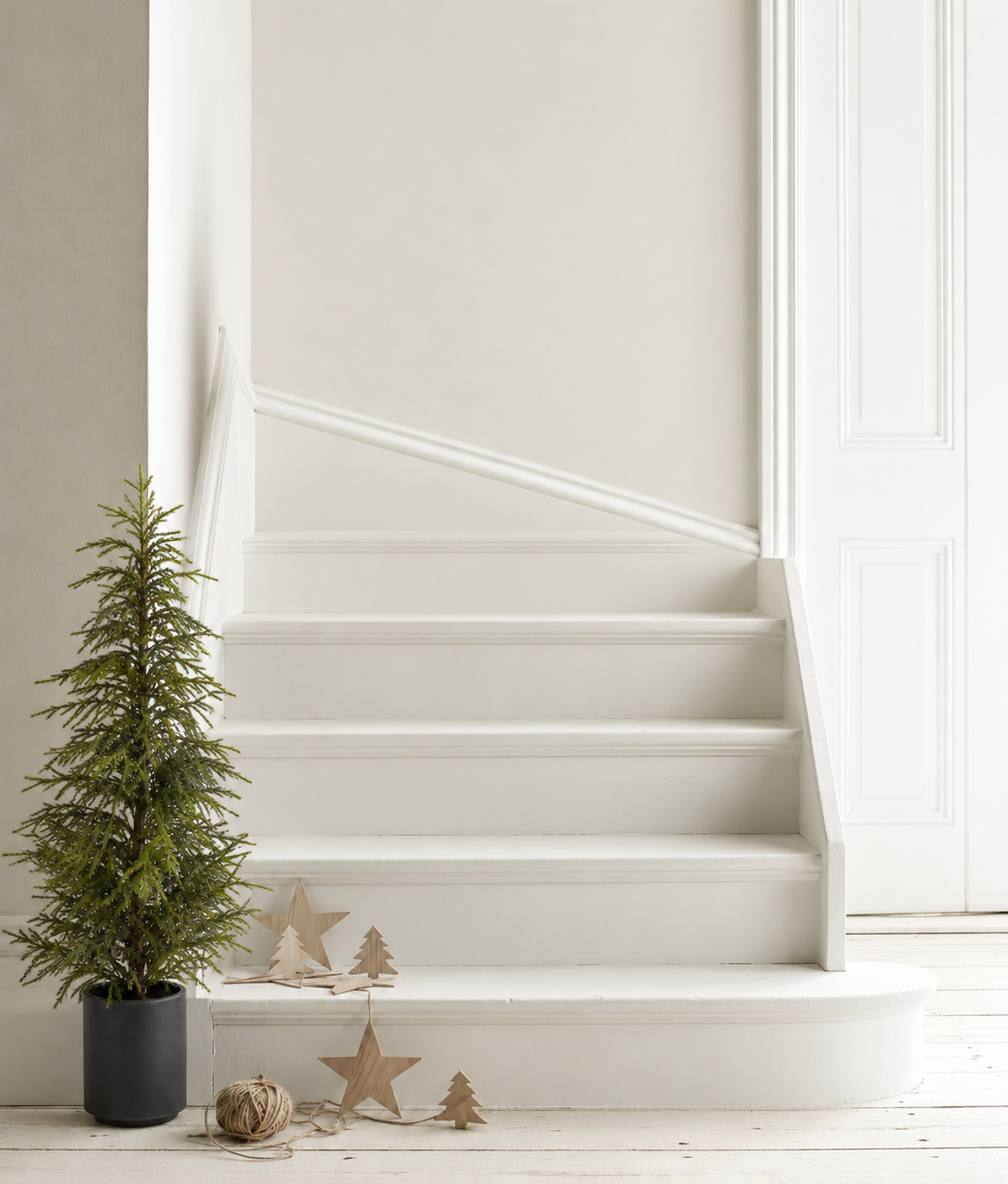 Soft pine potted tree in a black pot at the foot of a white staircase with wooden star decorations