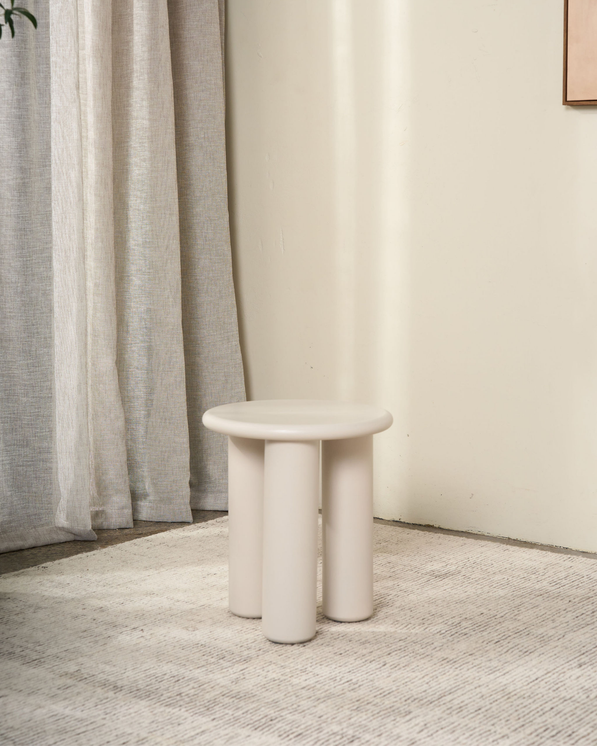 Cream side table on a pale rug beside linen curtains