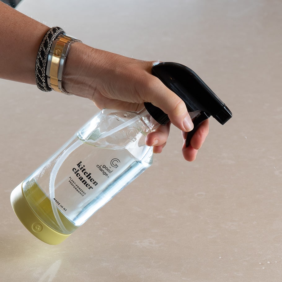 A person holding a Good Change reusable glass spray bottle at a kitchen bench.