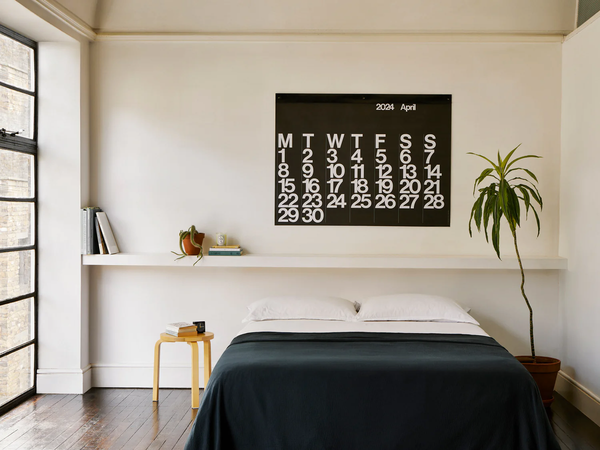 Stendig Calendar by Massimo Vignelli in its white on black April layout above a bed in a minimalist bedroom