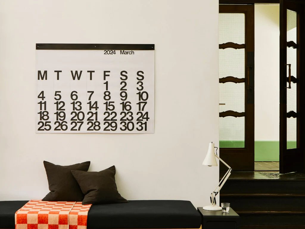 Stendig Calendar by Massimo Vignelli above a black daybed with cushions and a checkerboard throw in a sunlit living room