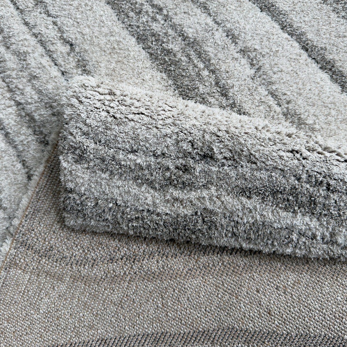 Folded corner showing the plush grey pile and the woven backing