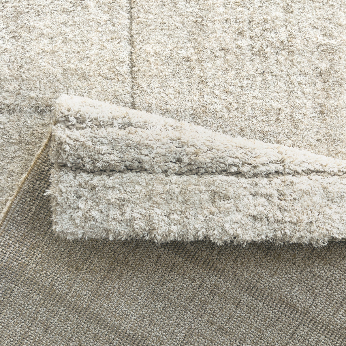 Folded corner of the beige rug showing the plush pile and woven backing