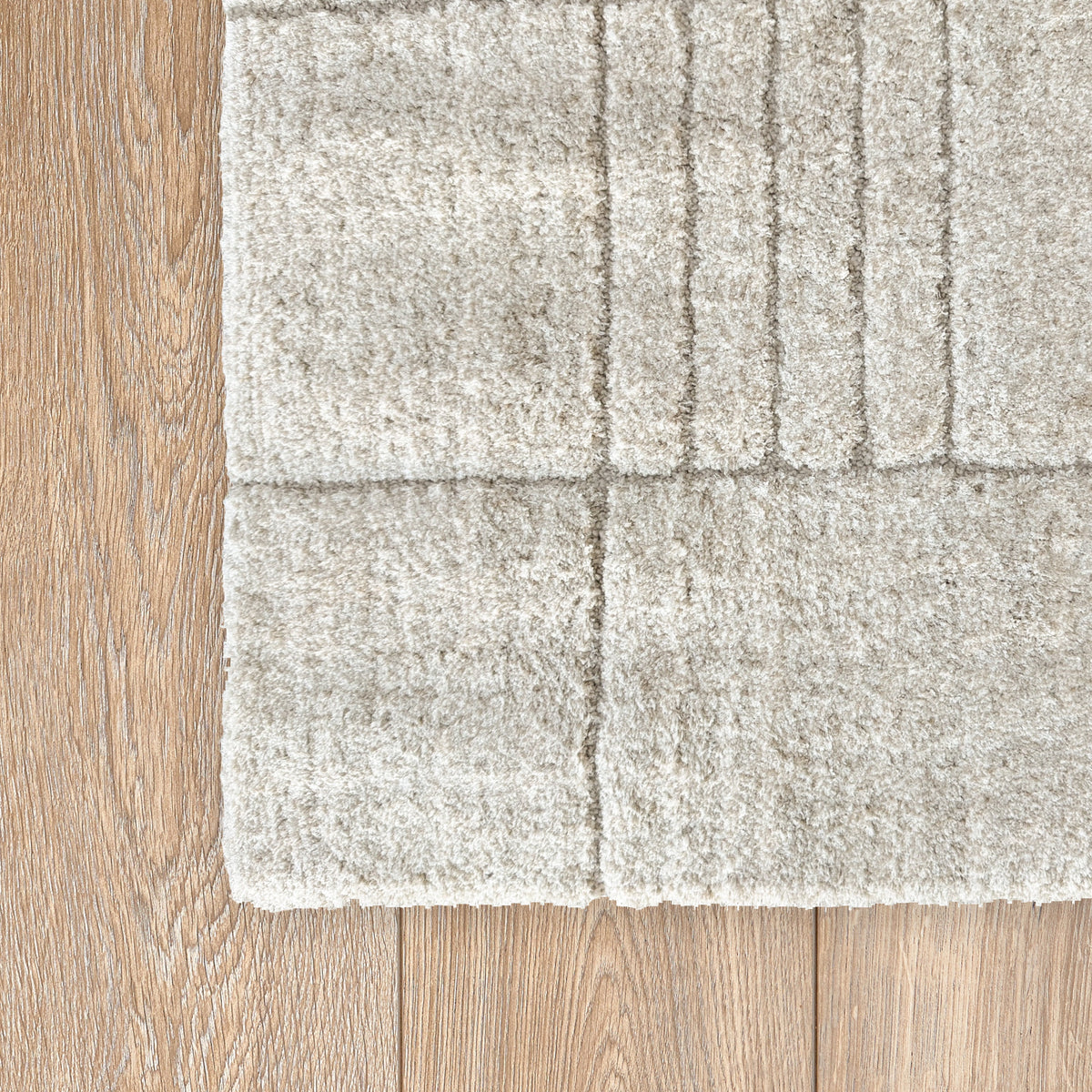Corner of the beige rug showing the line pattern on a timber floor