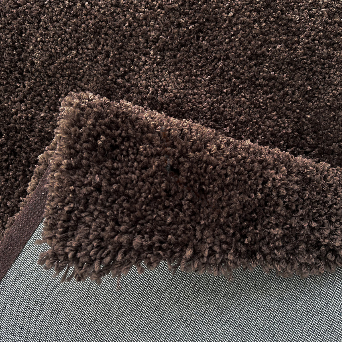 Folded edge of the acorn brown rug showing the pile depth and pale backing