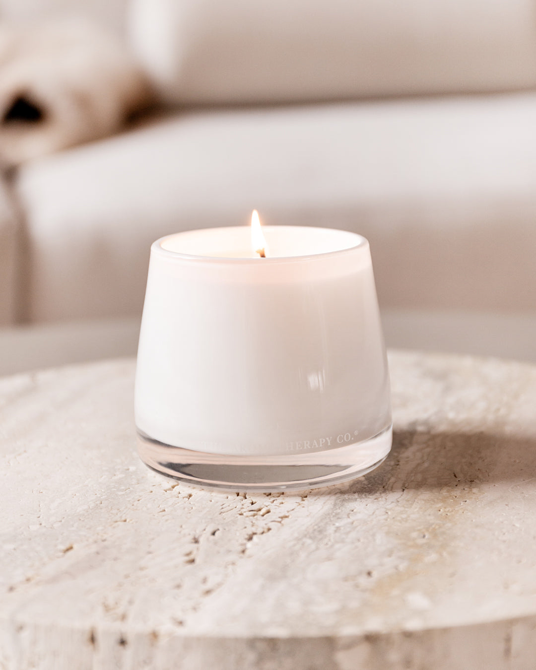 Lit Embrace candle on a round travertine side table in front of a cream sofa