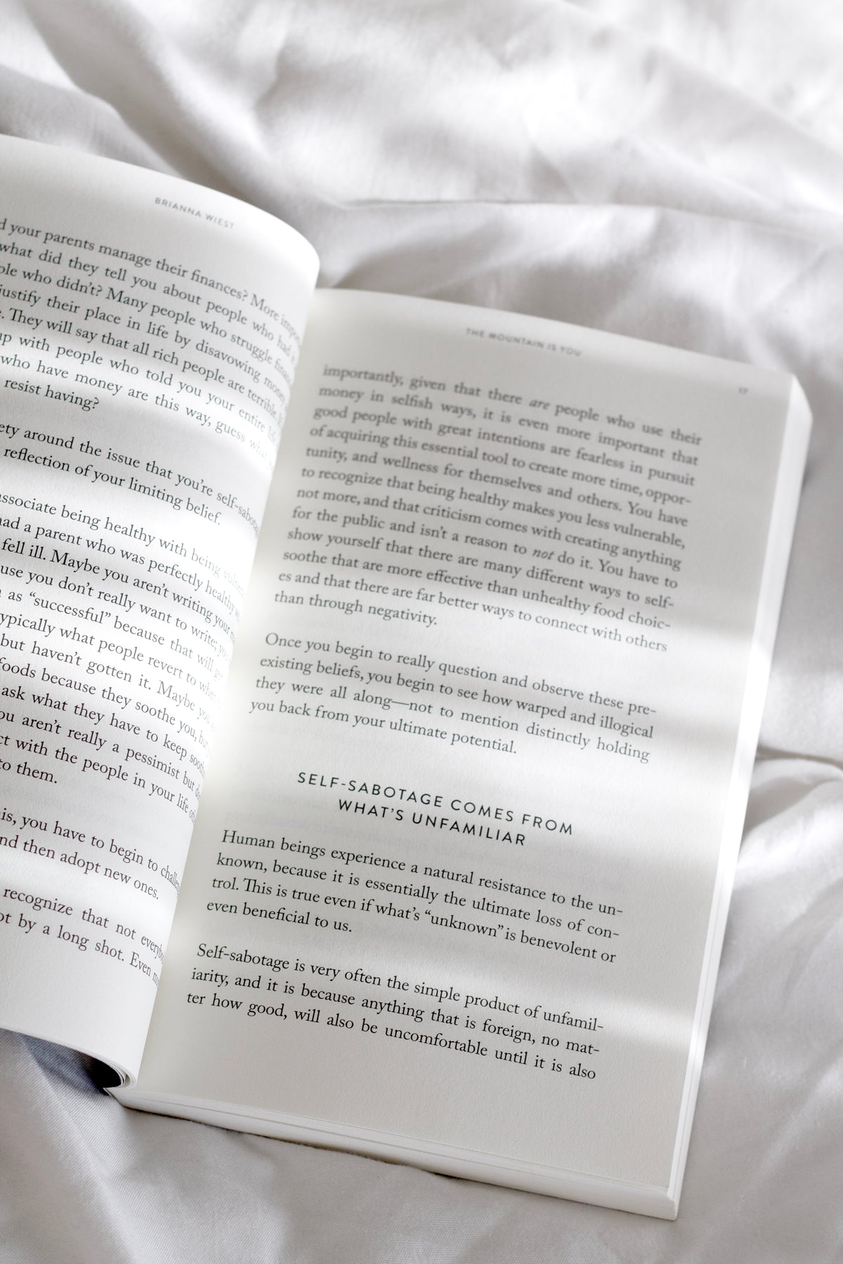 The Mountain Is You by Brianna Wiest open book on white bedding in soft neutral light