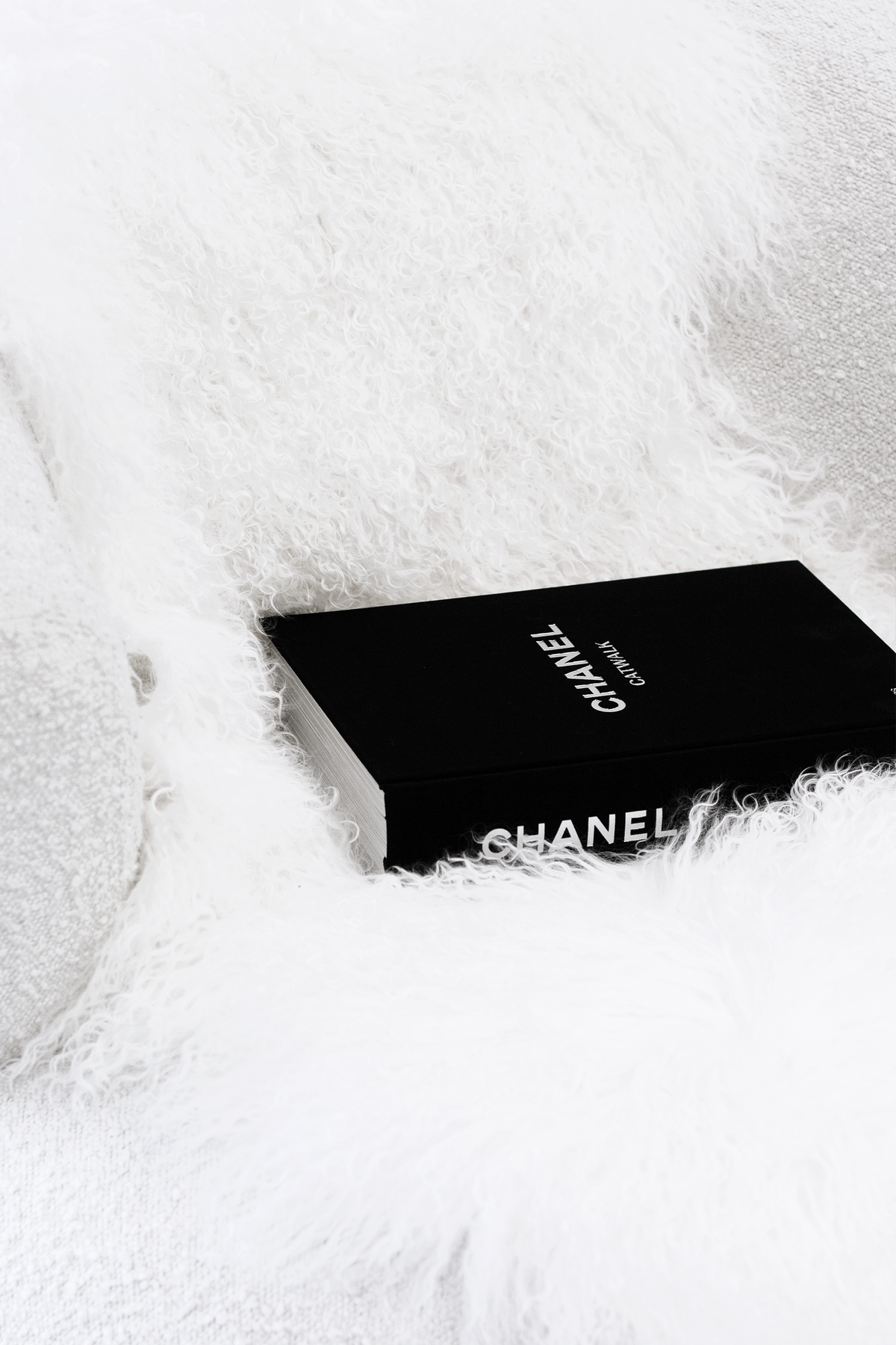 Close view of long white curly lamb fur with a black coffee table book resting on it