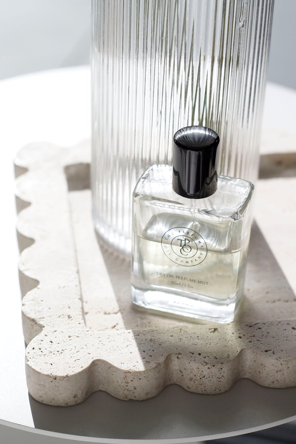 Perfume oil bottle on a travertine tray against ribbed glass