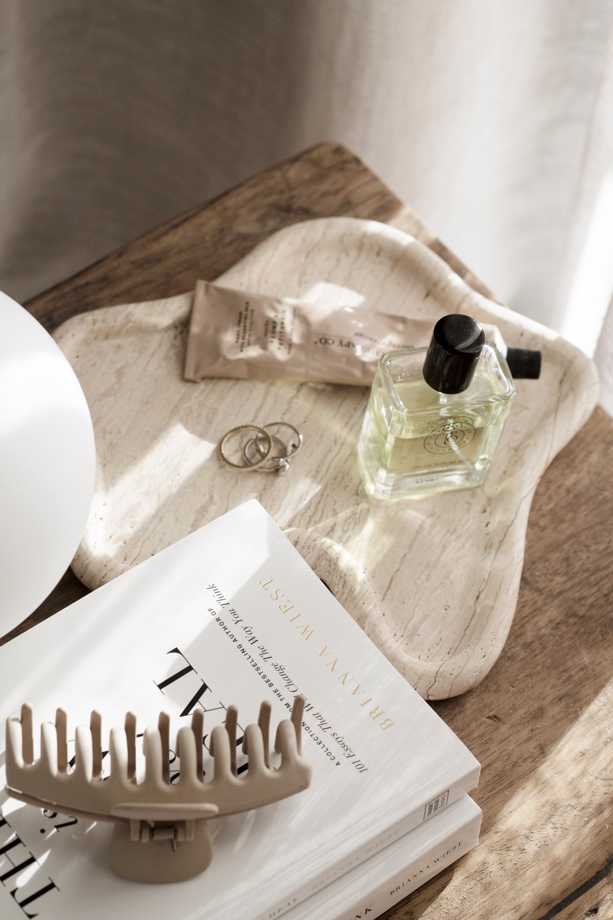 Travertine curved tray styled with perfume, jewellery and books on wooden bedside table