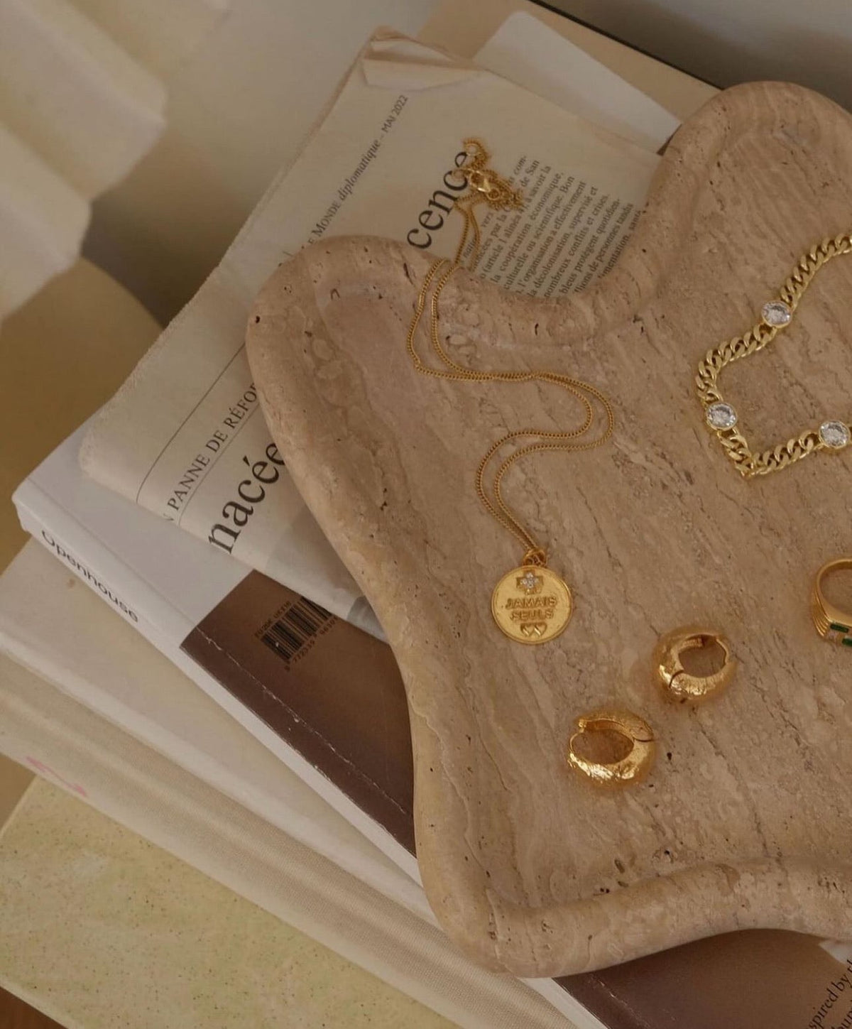 Travertine curved tray holding gold earrings on top of books, close view
