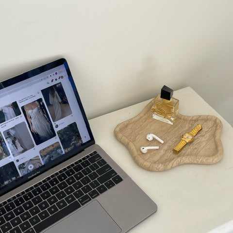 Travertine curved tray holding jewellery and earbuds beside a laptop