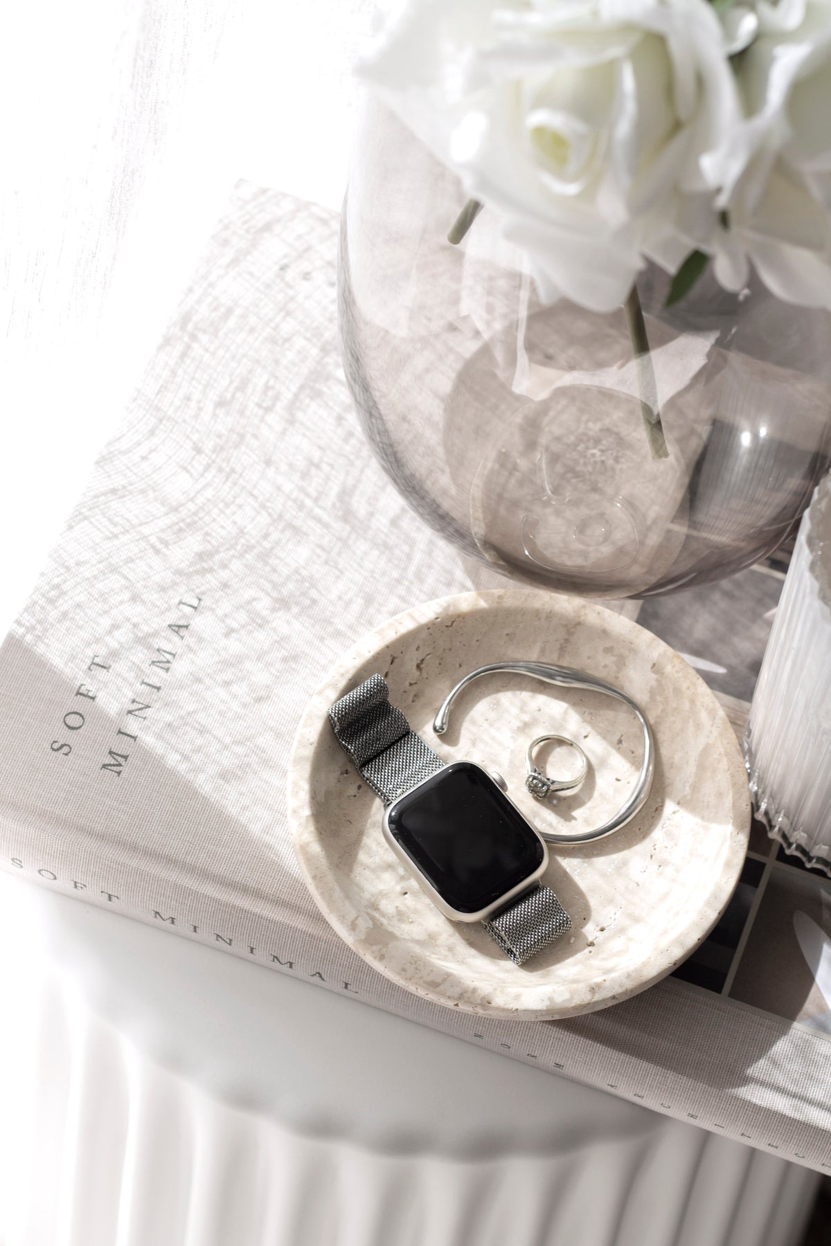 Overhead view of the travertine tray with a watch and rings, roses in a glass vase behind