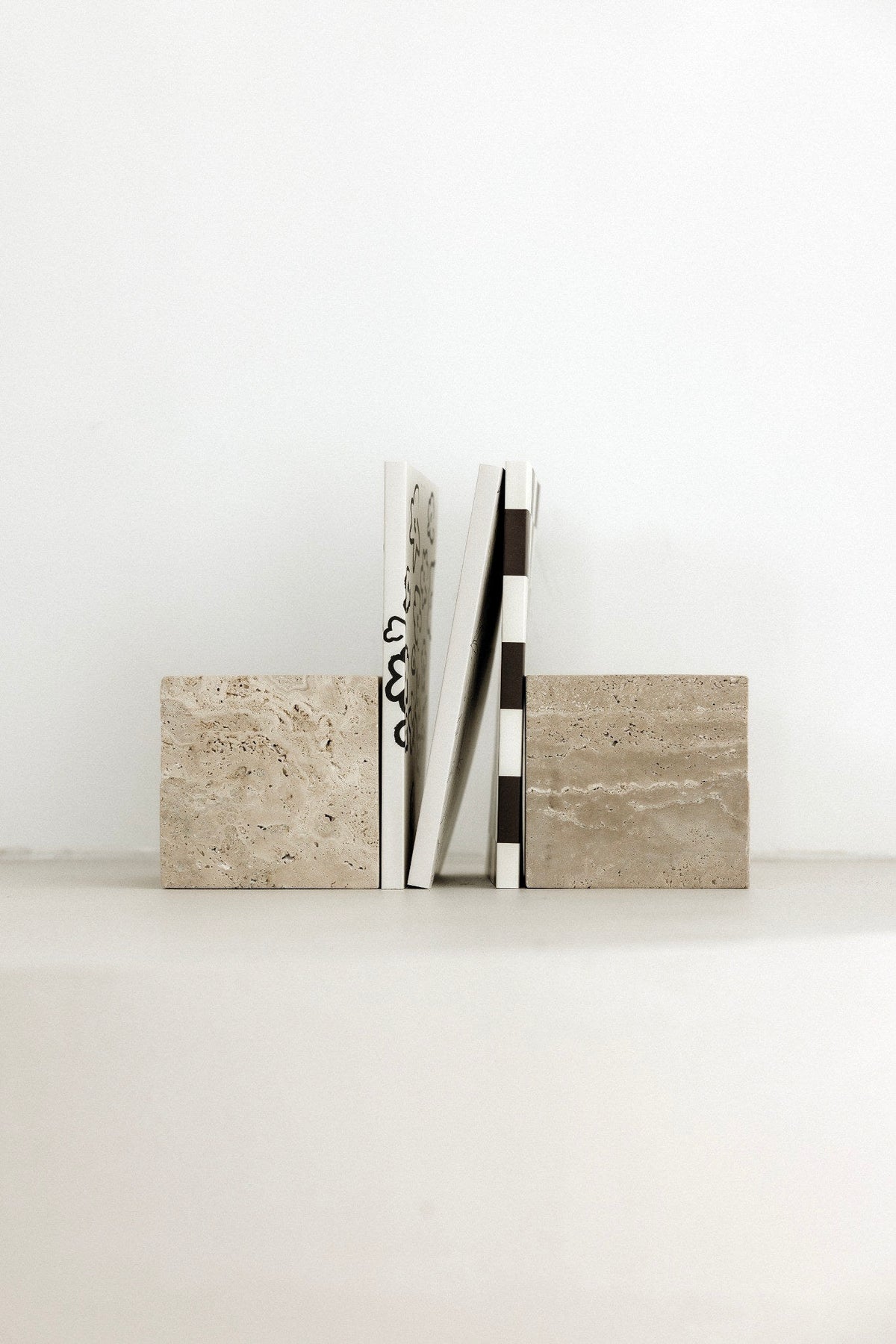Travertine stone bookends holding books on a pale shelf