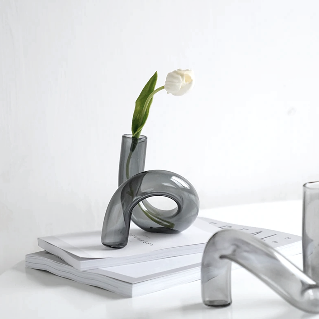 Smoke J-Curve vase holding a single white tulip on books, with a clear one lying alongside