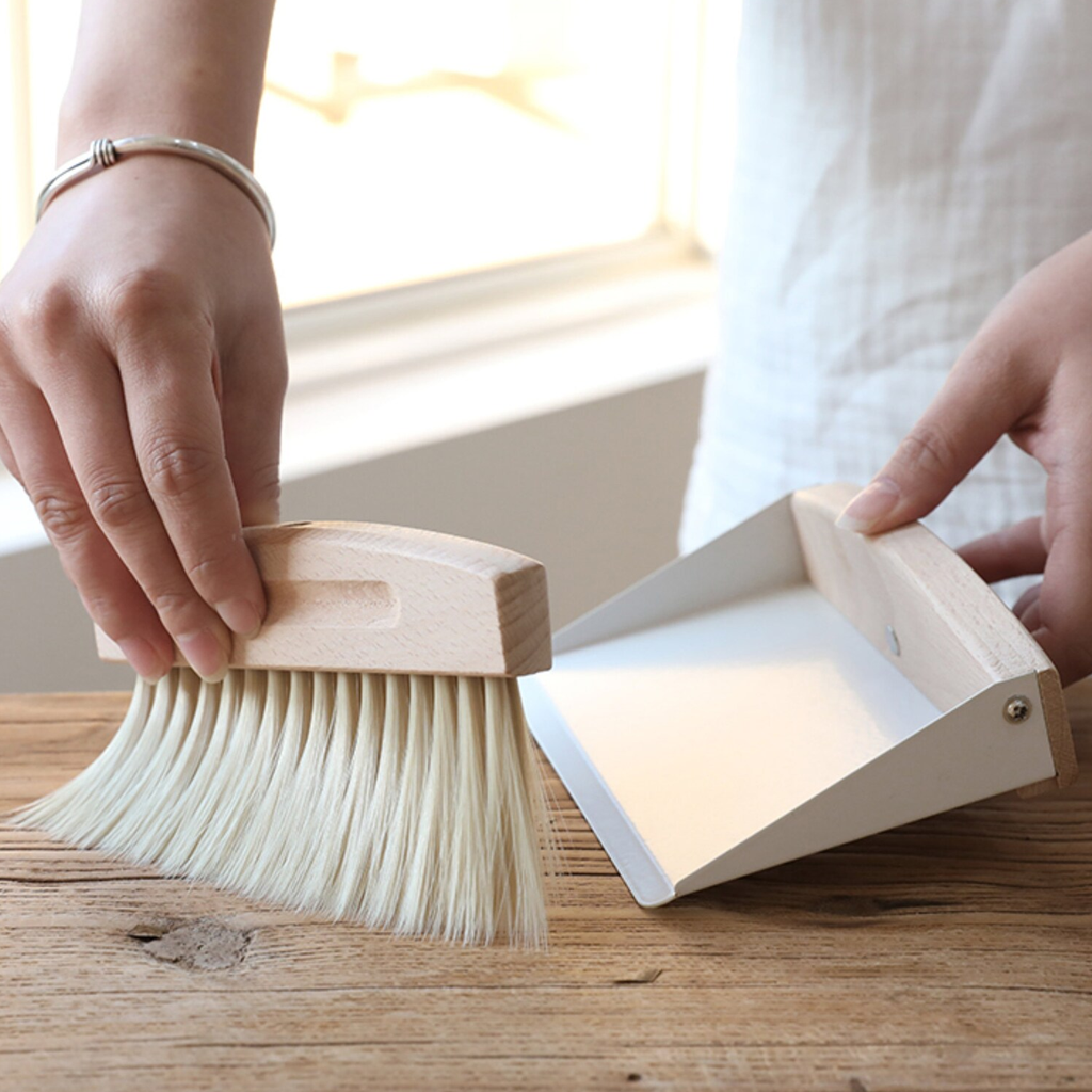 Sweeping dust from a wooden table into the tabletop dustpan beside a sunlit window
