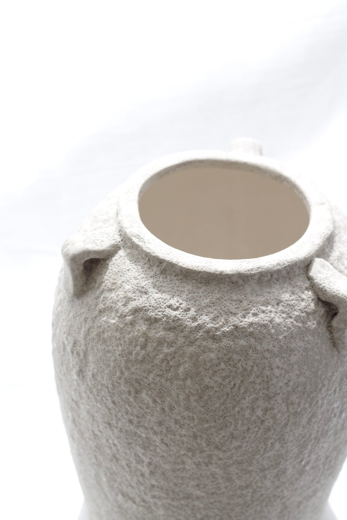 Close-up of the top of the sculptural beige vase showing raw textured finish and interior glaze