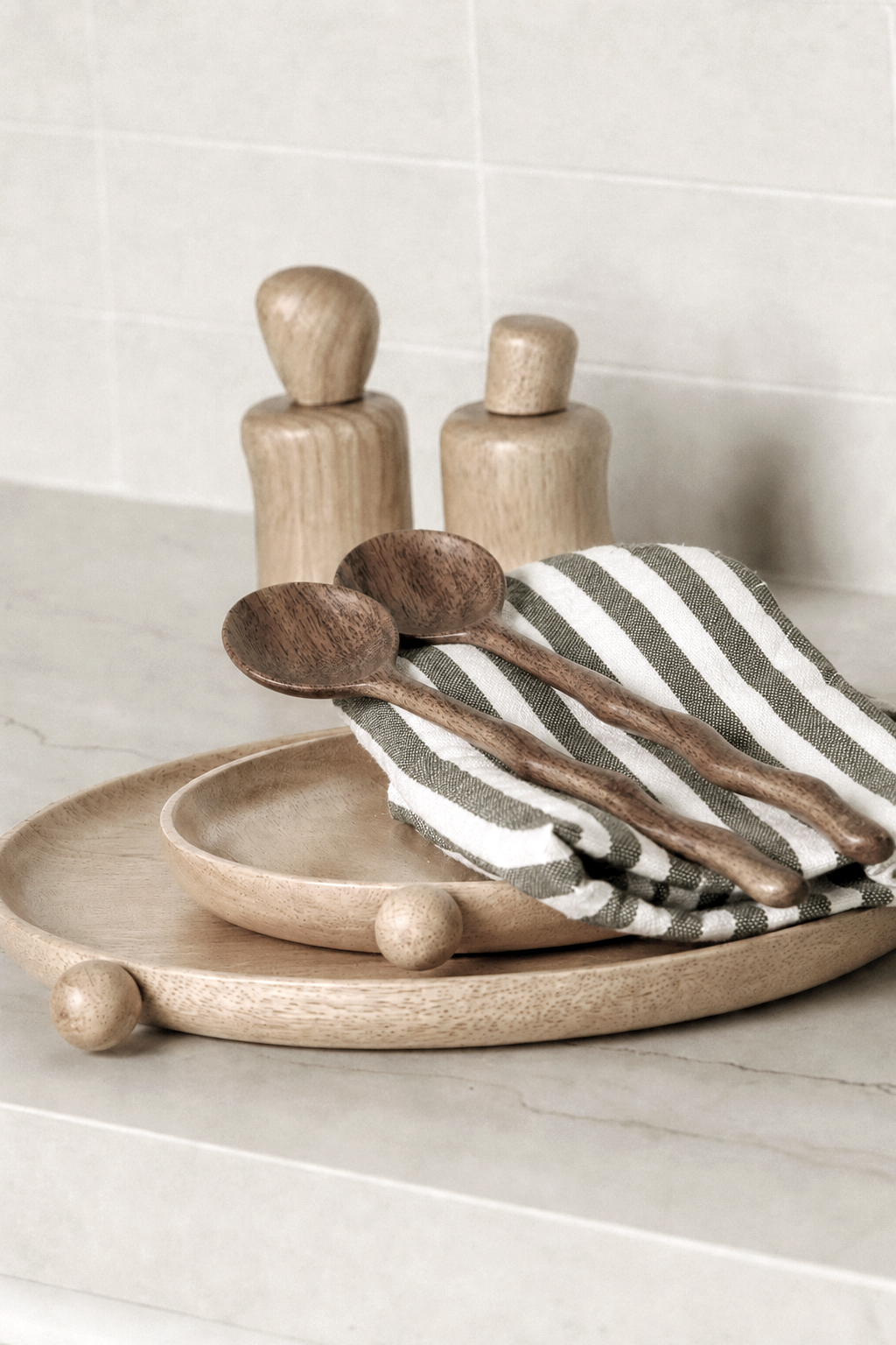 Natural wavy salt and pepper shakers beside wooden salad servers and a round wooden tray