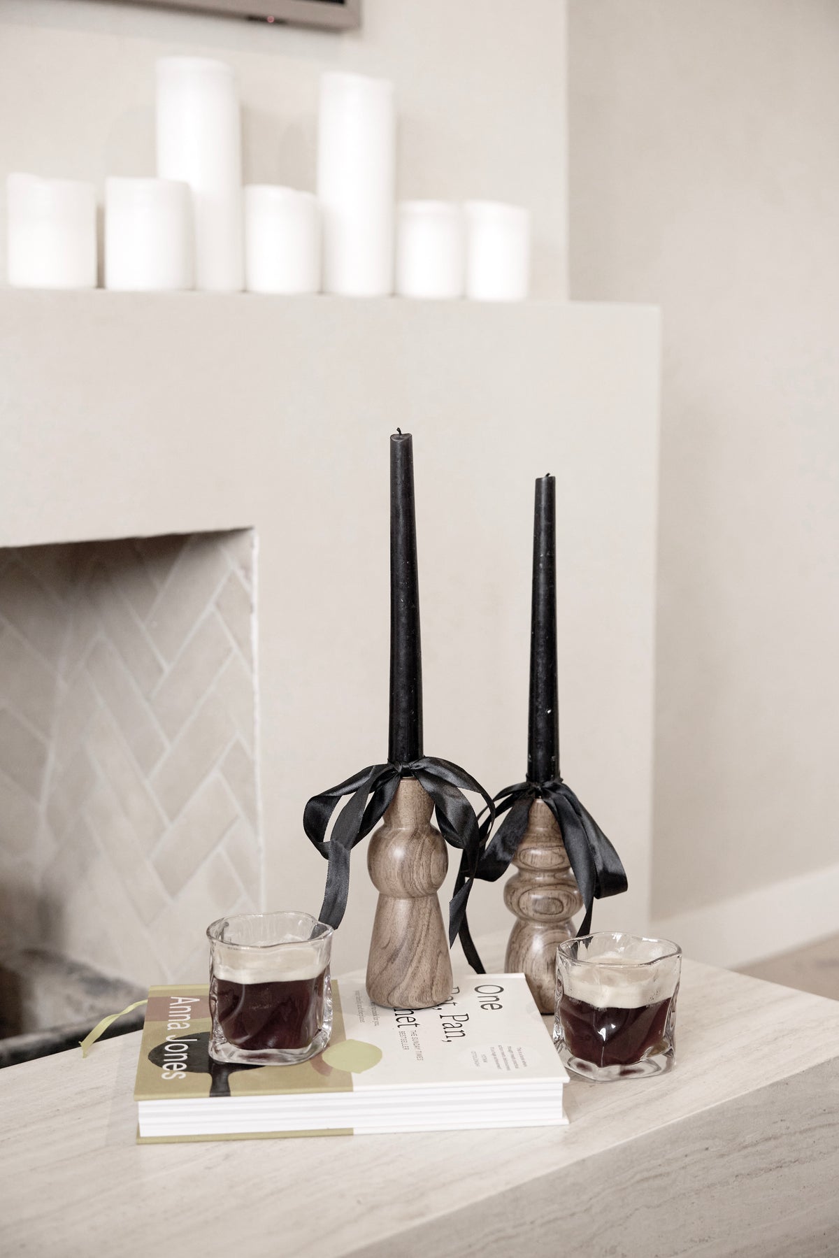 Wavy textured glasses on a book beside black candles and a fireplace