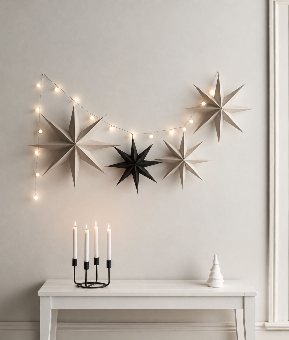 White minimalist terracotta tree on a white bench beside a black candle holder under paper stars