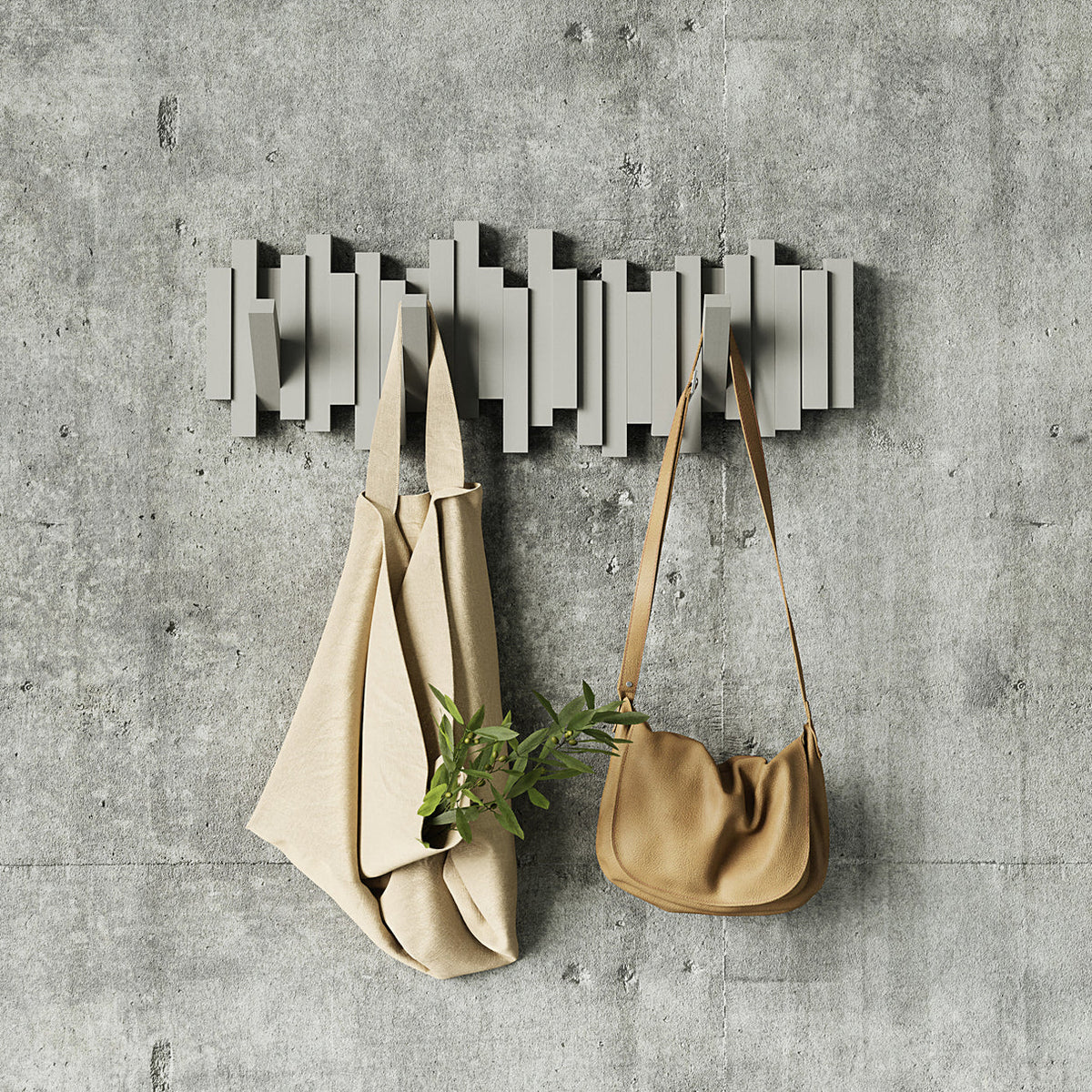 Umbra Sticks 5 hook rack in grey on a concrete wall with a coat and a tote bag