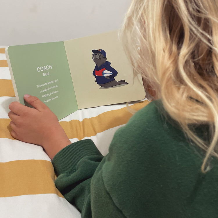 Child turning the pages of Wild About Footy, seen over her shoulder
