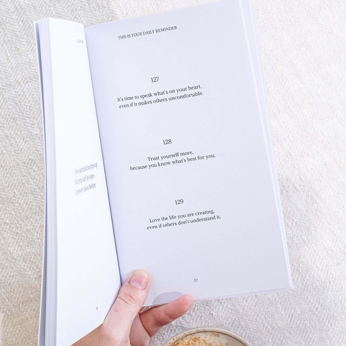 Hand holding the book open at reminders 127 to 129, each set in simple serif type on a white page