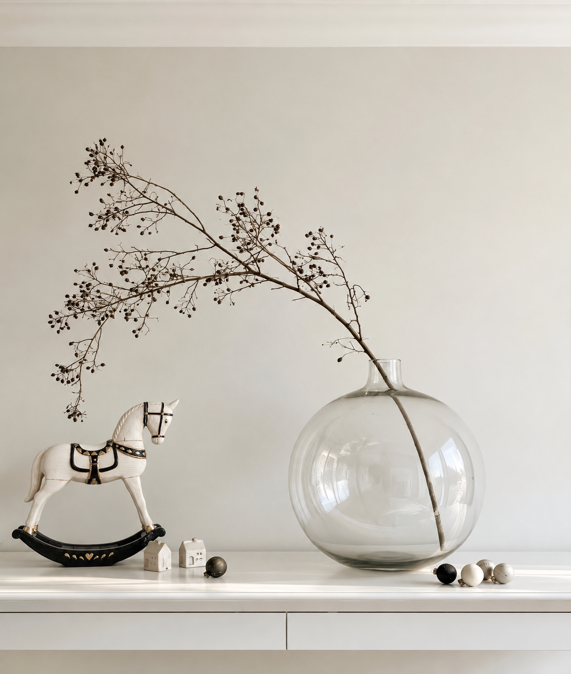 White rocking horse Christmas ornament with black rockers on a white sideboard beside a glass vase