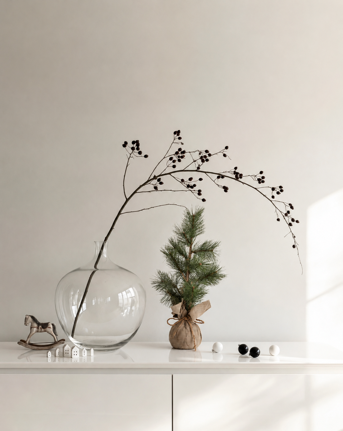 Long Needle Pine Tabletop Tree in burlap on a white sideboard beside a glass vase with a berry branch