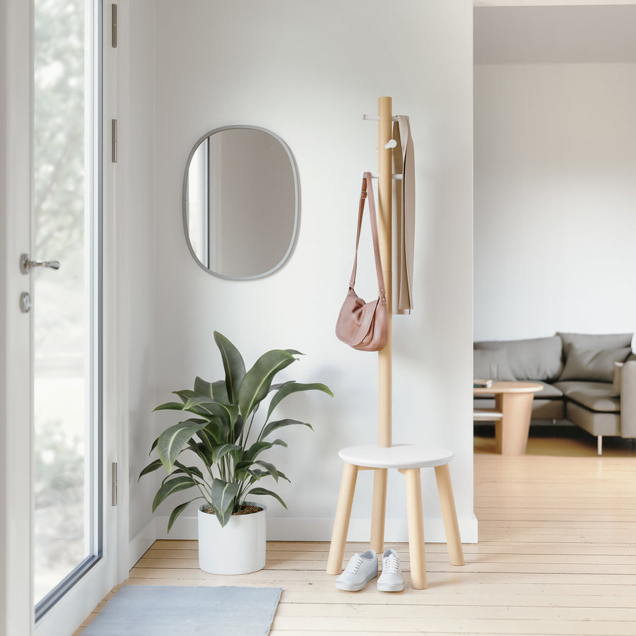 Umbra Pillar coat rack in natural in a bright entryway beside a plant and mirror