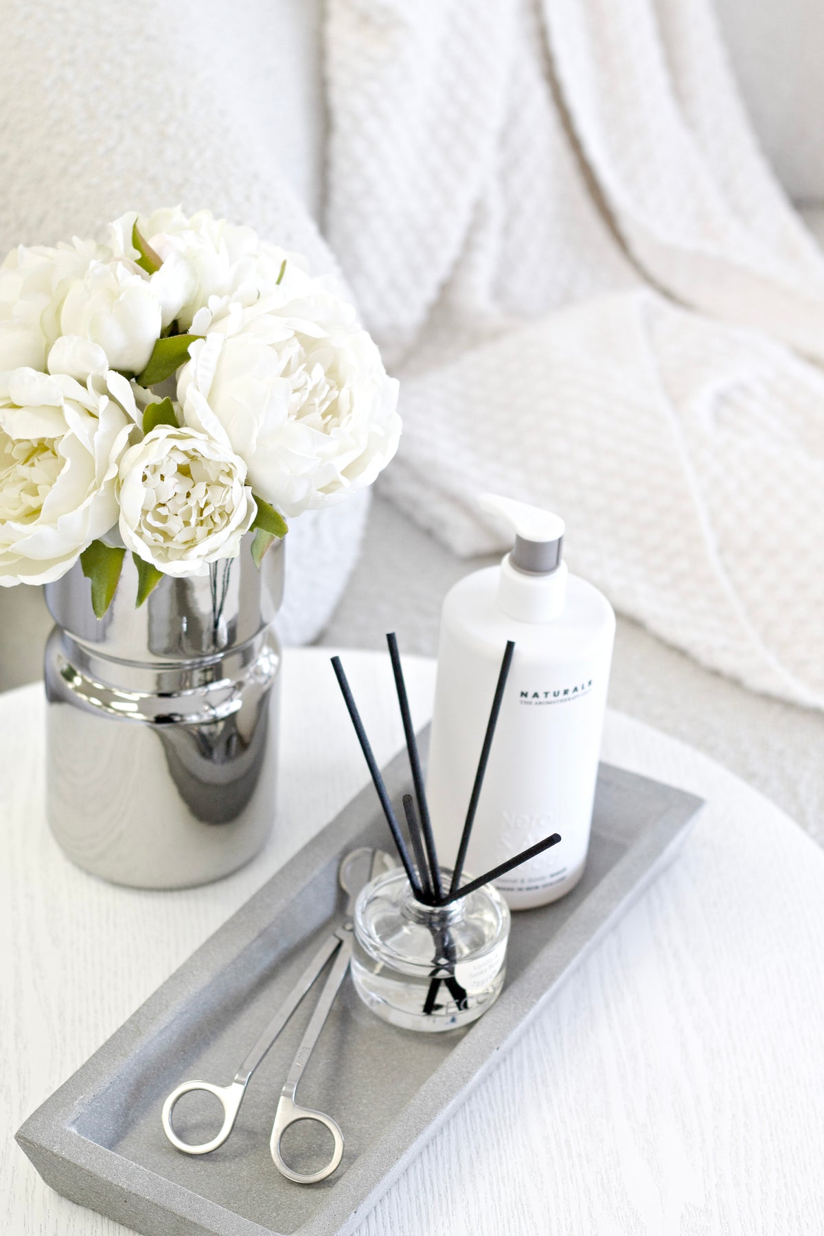 Zakkia natural concrete tray with a diffuser, lotion bottle and silver vase of white flowers