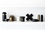 A black shelf with Zakkia Concrete Cross Trivet - Black and gold vases and a cactus.
