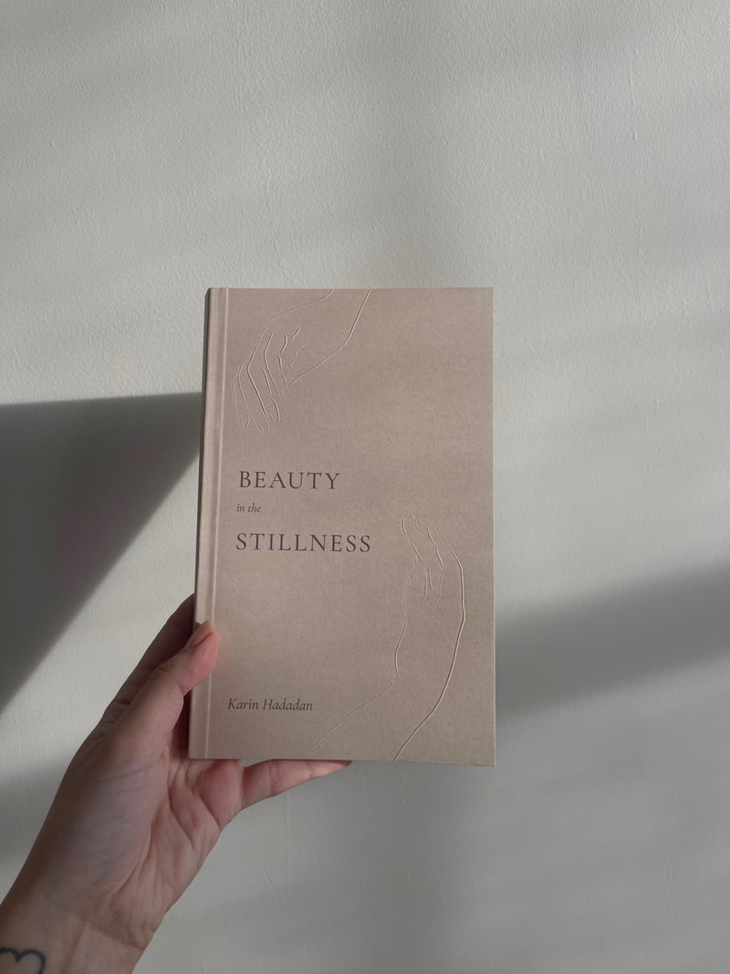 A hand holding a book that says Beauty in the Stillness by Thought Catalog.