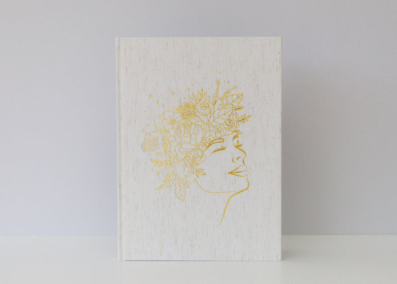 A Olive + Page Joy Journal for busy Mamas, with a white book featuring a woman's head on it.