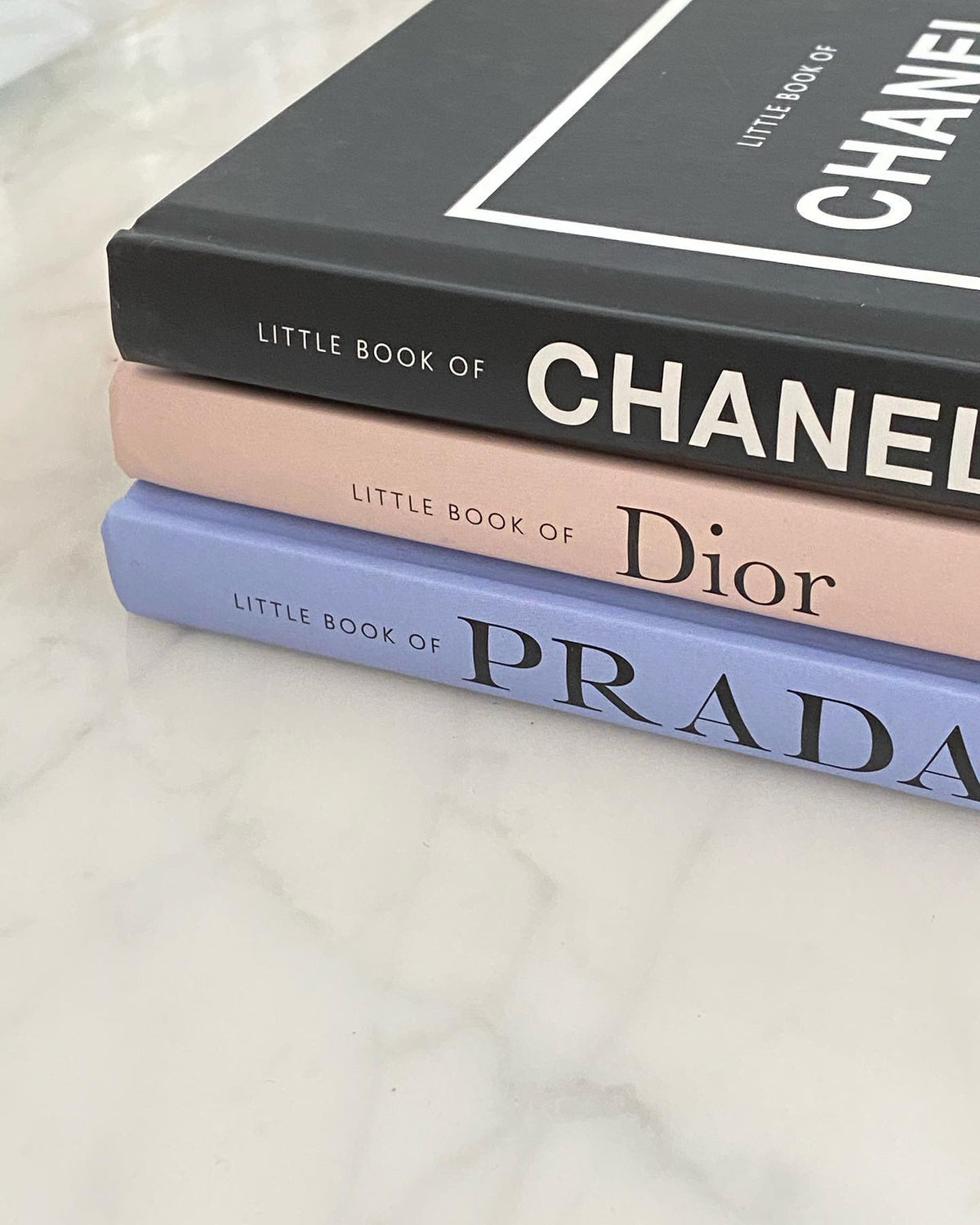 Little Book of Chanel stacked with Little Book of Dior and Little Book of Prada on marble