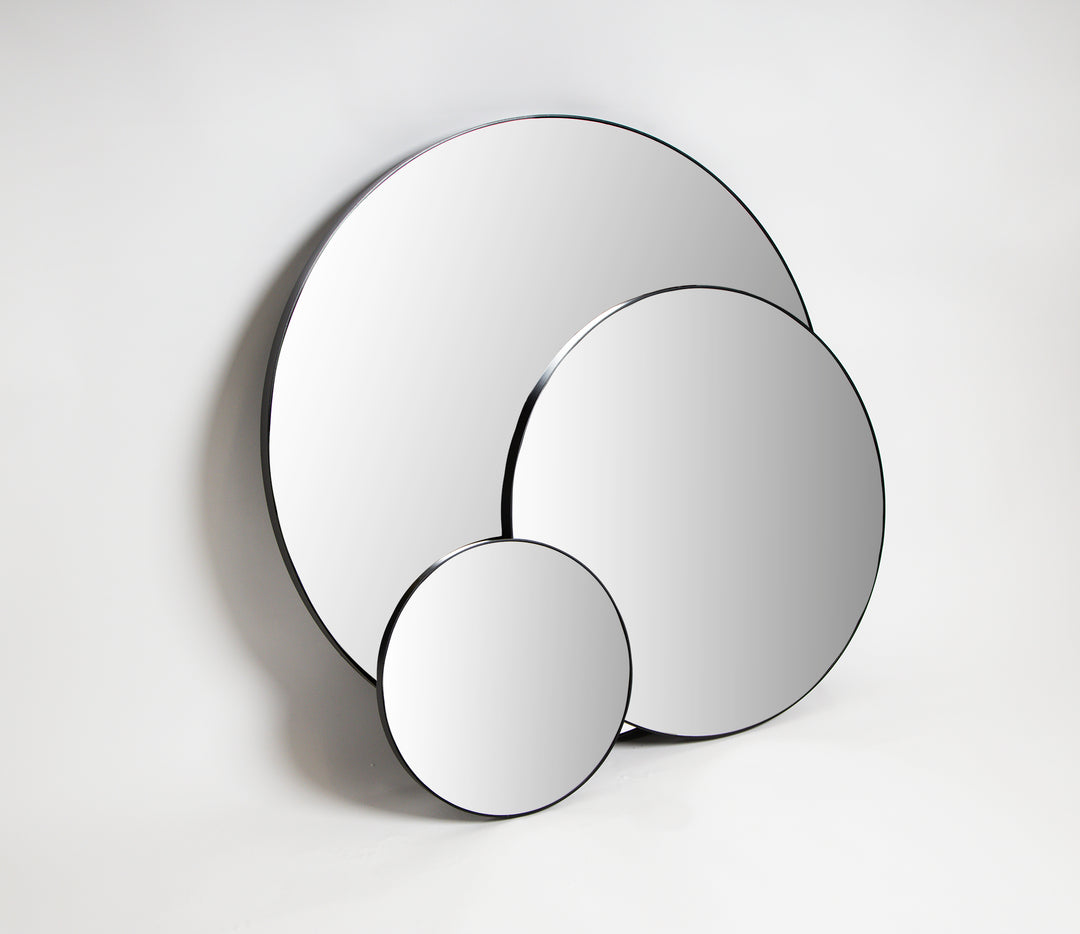 Three round black frame mirrors in different sizes overlapping against a pale grey wall