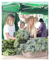 Two women and a child buying Raw & Free plant-based vegetables at an outdoor market.