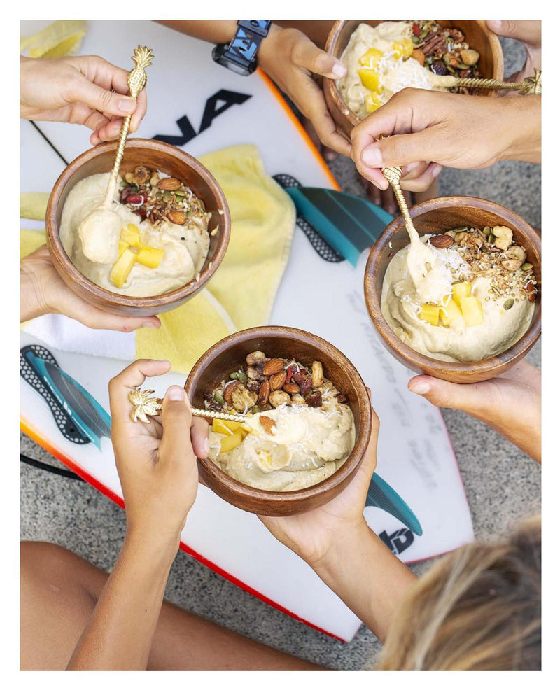 A group of people holding bowls of Raw & Free ice cream with surfboards in the background, showcasing a vibrant Books lifestyle.