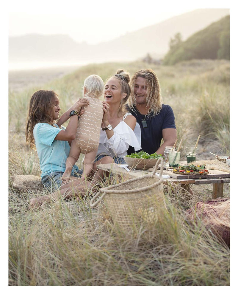 A family enjoys a picnic on a Raw & Free blanket in the sand.