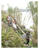 A group of people carrying Raw & Free surfboards up a set of stairs at the beach.