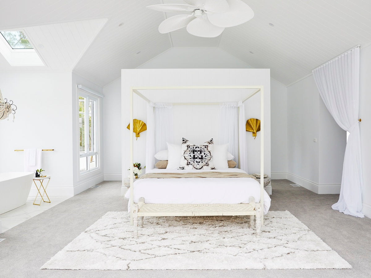 White canopy bed on a patterned rug under a vaulted ceiling