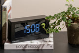 A Scandinavian Karlsson clock sitting on a table next to a potted plant.