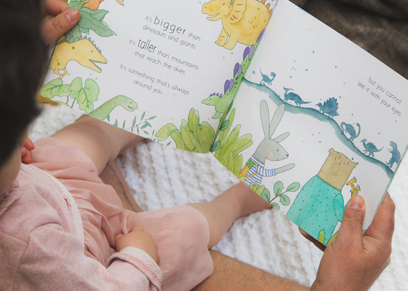 A baby is embarking on a magical adventure while reading "IN A WORLD FULL OF MAGIC" by Olive + Page, a book about dinosaurs.