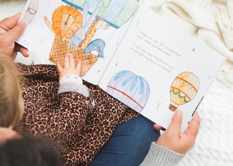 A child is reading the book MY WISHES FOR YOU by Olive + Page about hot air balloons.