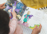 A little girl is reading IN A WORLD FULL OF MAGIC, by Olive + Page.