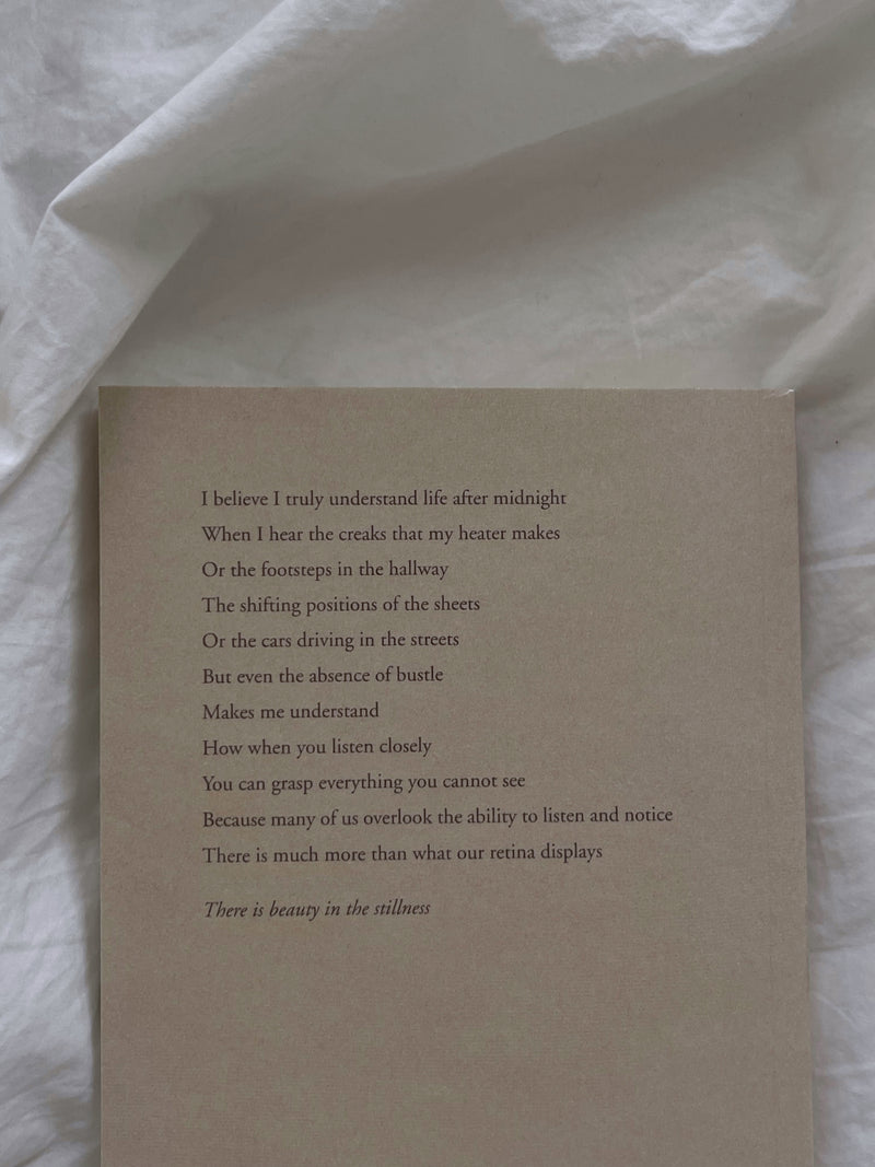 A "Beauty in the Stillness" book by Thought Catalog with a poem on it sitting on a bed.