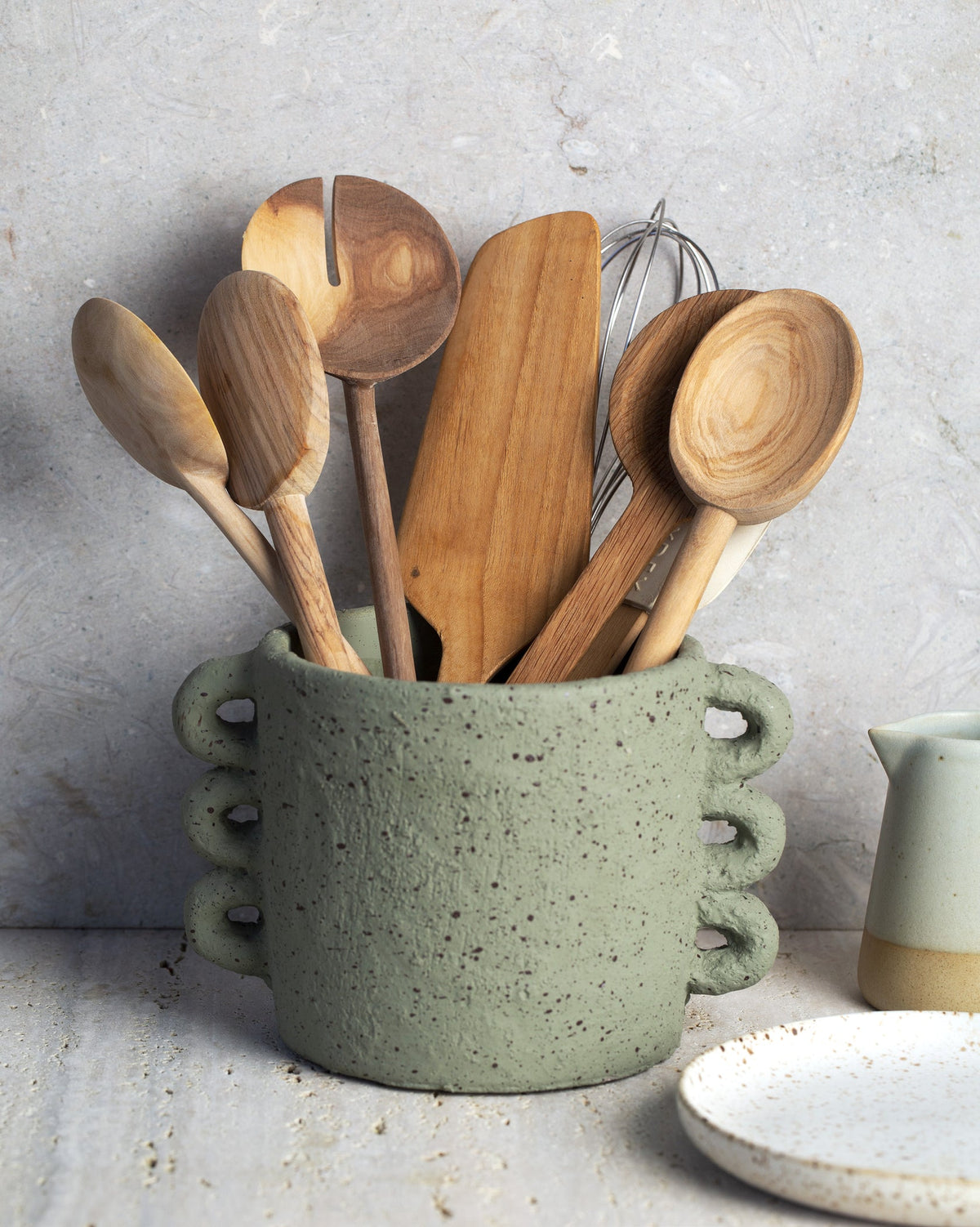 A green bowl with wooden utensils, perfect for Simple Wholefoods enthusiasts looking for design and lifestyle inspiration by Sophie Steevens's book "Simple Wholefoods | 100 Effortlessly Delicious Plant Based Recipes for Everyday".