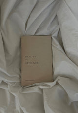 A book with the title "Beauty in the Stillness" by Thought Catalog laying on a bed.